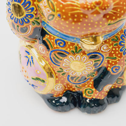 Close-up of the lucky cat's chest showing its blue collar, gold-tone bell, white flower, pink side panel and black paws.