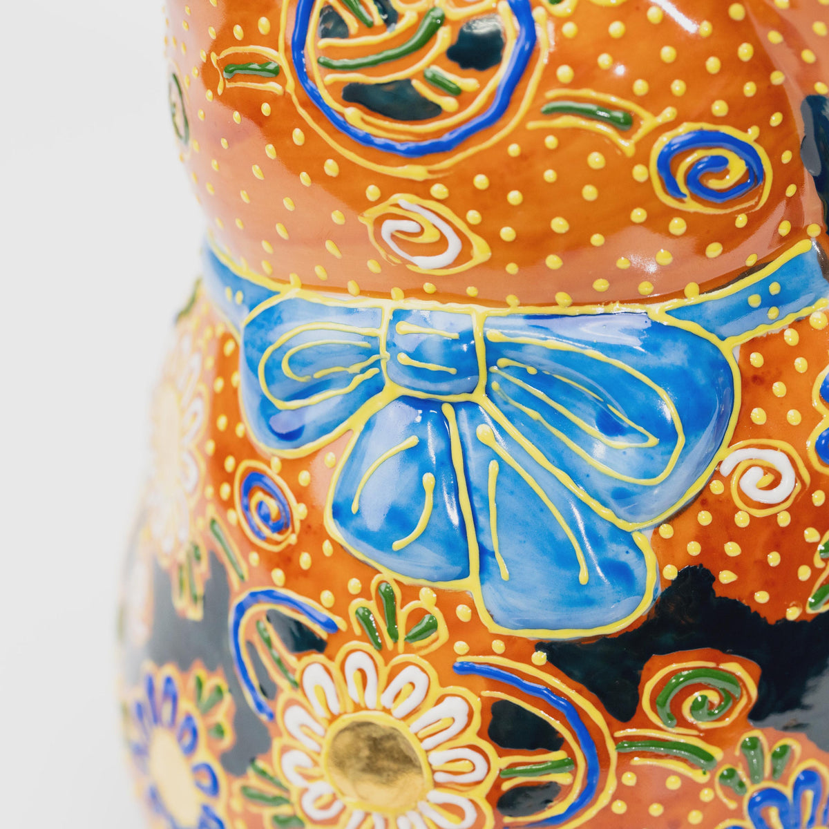 Close-up of the large blue bow at the back of the collar, outlined in raised yellow against copper-orange glaze.