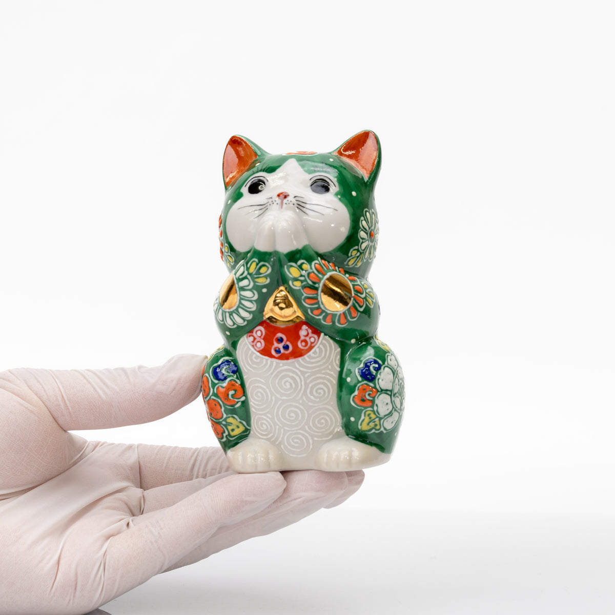 Green Kutani praying cat held in a gloved hand to show its compact size.