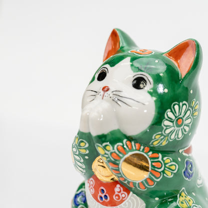 Close-up of the green cat’s white face and joined paws, orange ears, and raised floral decoration.