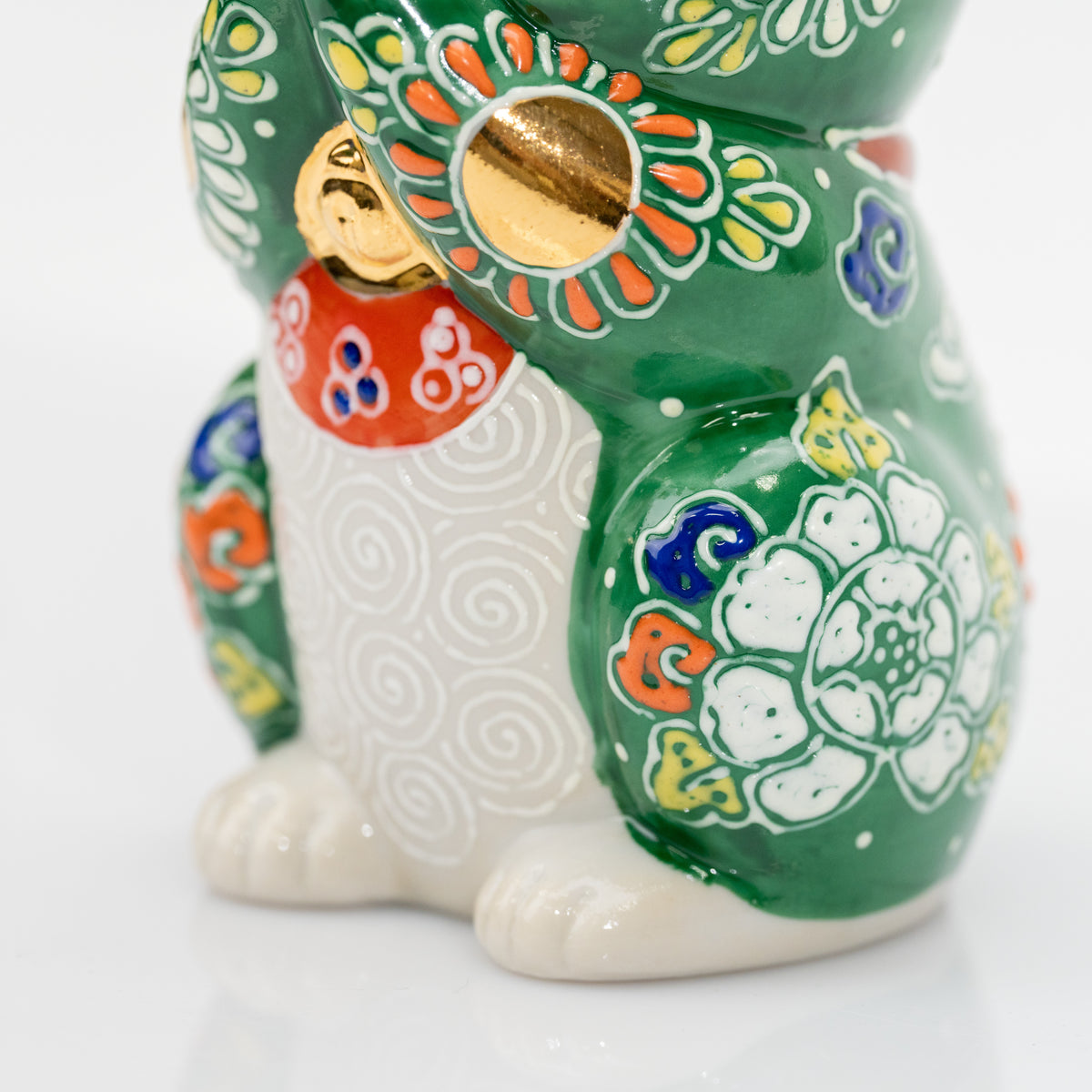 Detail of a gold-colored paw circle, red bib, white belly spirals, and a raised white flower on the green cat.