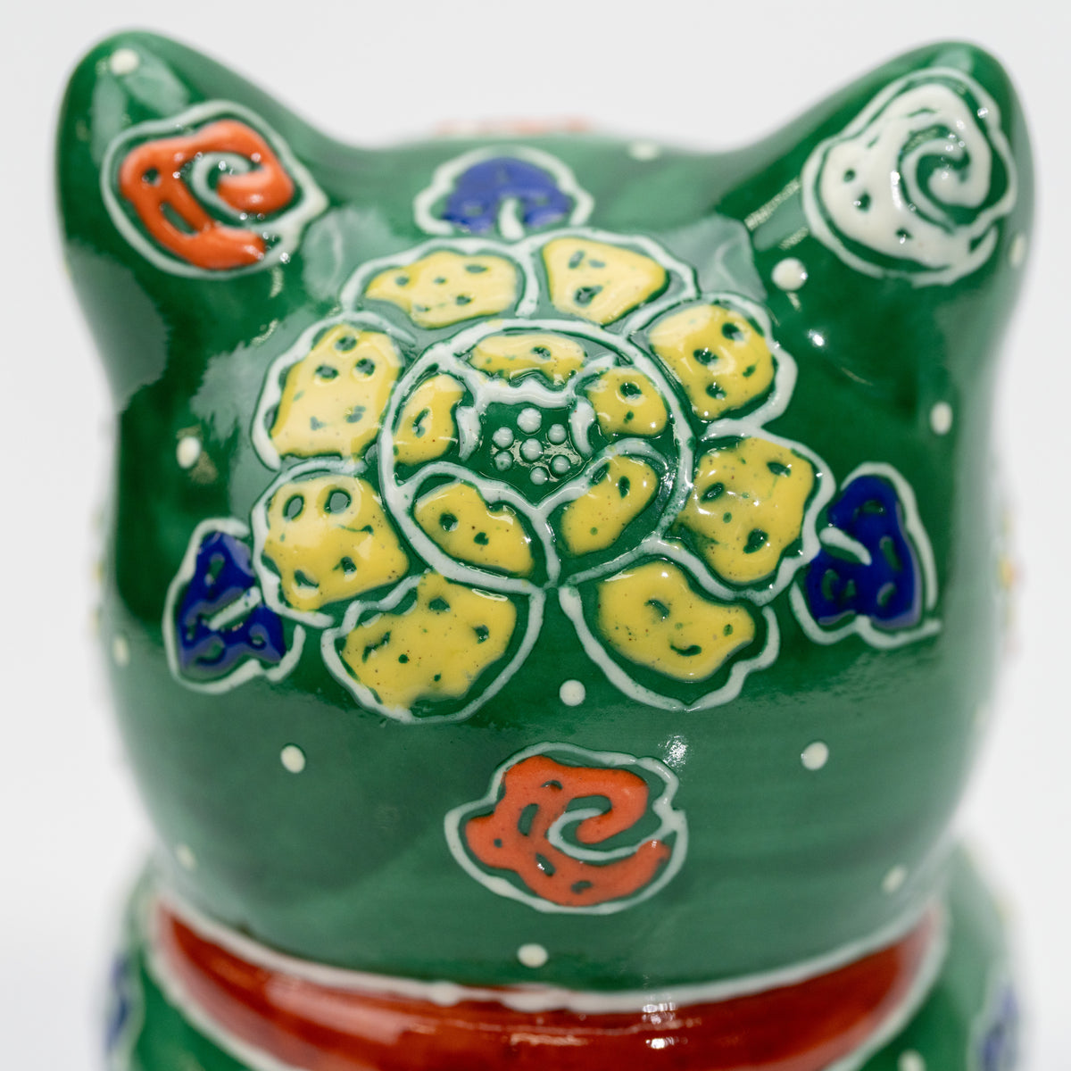 Detail of the yellow flower and blue curled motifs on the back of the green cat’s head.