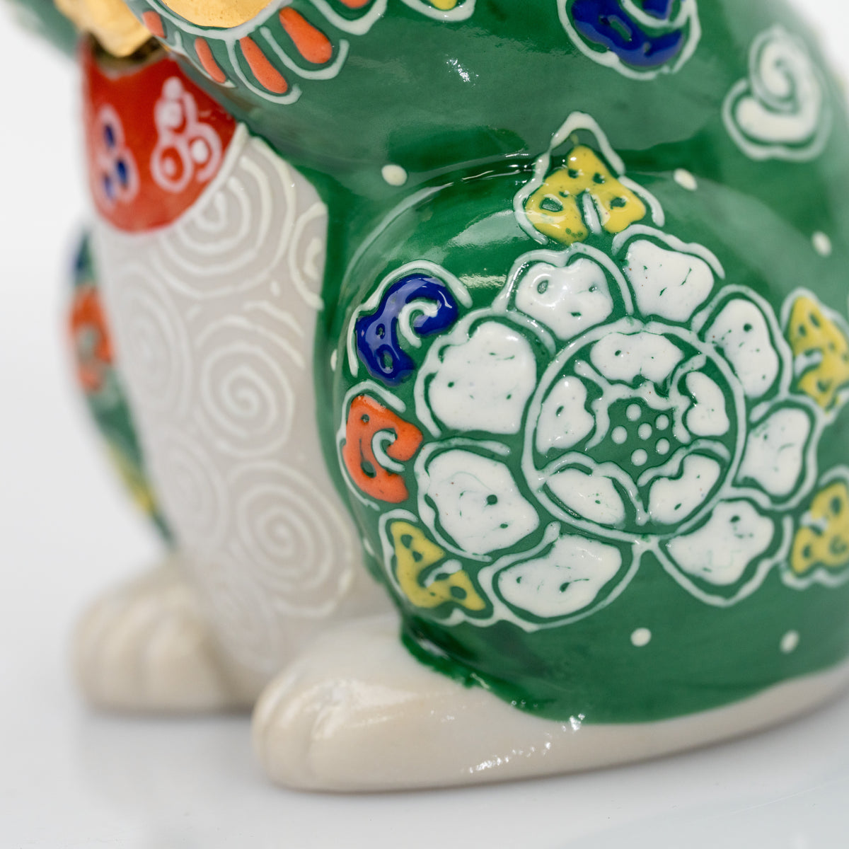 Detail of a white flower, yellow and blue motifs, and glossy green surface on the porcelain cat.