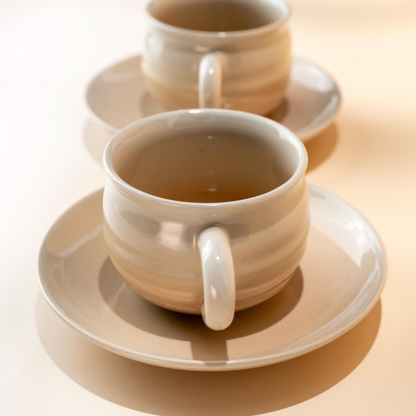 Angled view of a handmade Hagi yaki coffee cup resting on its saucer