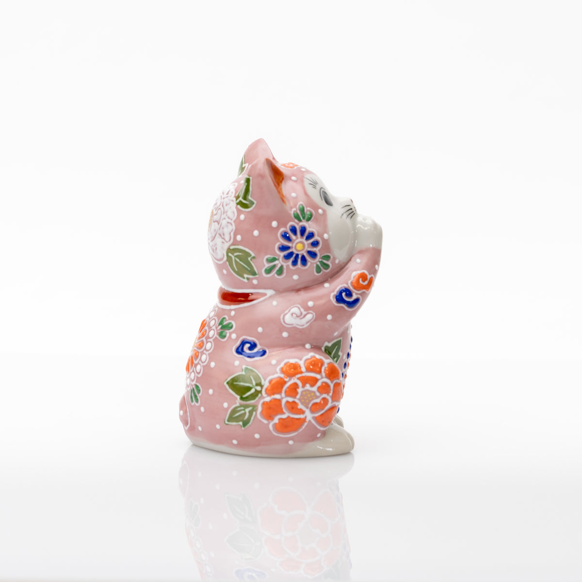 Side view of the pink ceramic praying cat with raised white floral outlines and green leaves.