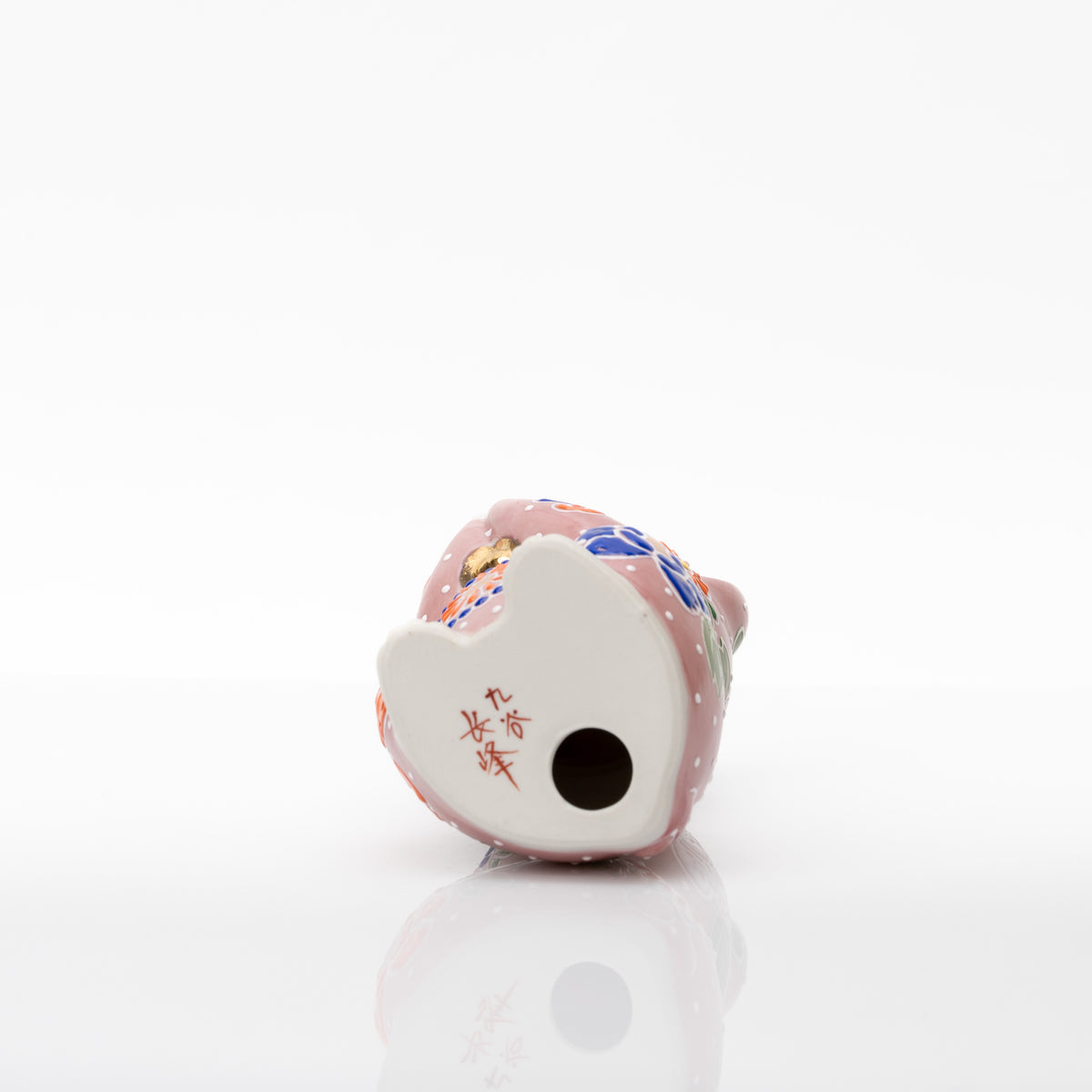 Underside of the pink ceramic cat showing the red 九谷 長峰 base mark and a round opening.
