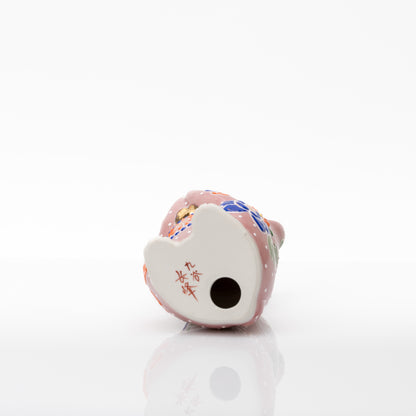 Underside of the pink ceramic cat showing the red 九谷 長峰 base mark and a round opening.