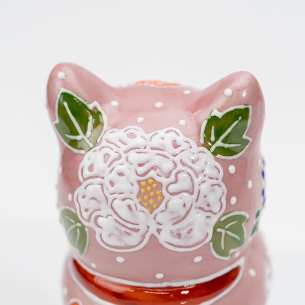 Close-up of the raised white flower and green leaves on the back of the pink cat’s head.