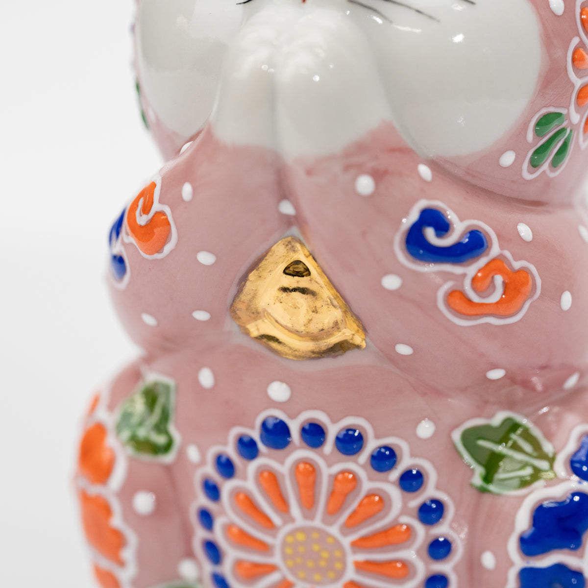 Close-up of the gold-colored chest accent between the pink cat’s joined paws.