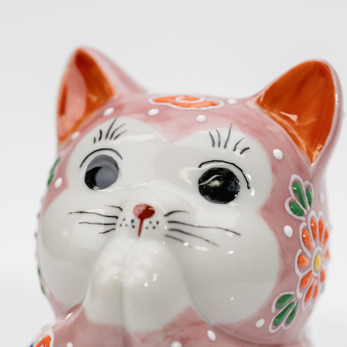Close-up of the praying cat’s white face, black eyes, orange ears, and pink dot-patterned head.