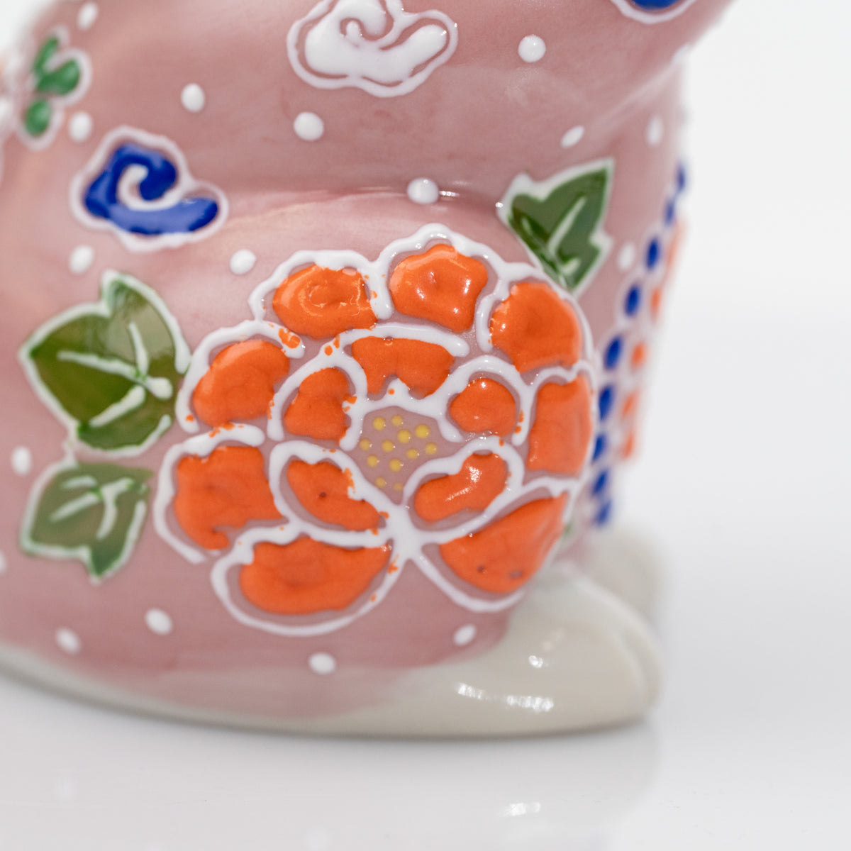 Close-up of an orange side flower, green leaves, and raised white dots on the pink cat.