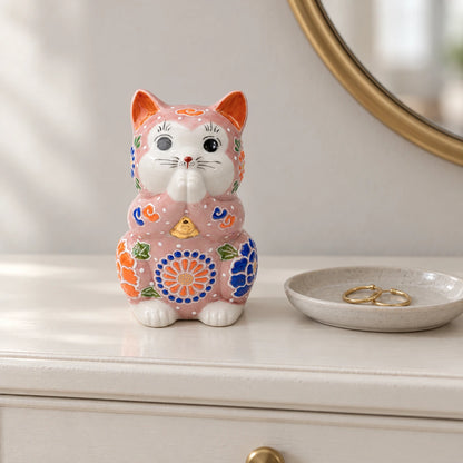 Pink floral Kutani praying cat on an ivory dressing table beside a small dish holding gold hoop earrings.