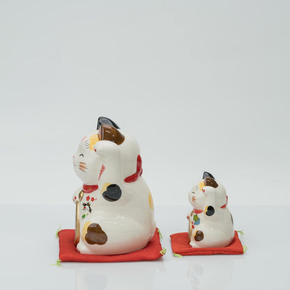 Side view of the 15 cm and 8.5 cm calico lucky cats on red cushions