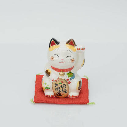 Front view of the stationary 8.5 cm calico lucky cat with raised left paw on a red cushion
