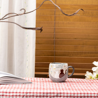 Kutani Hidamari cat mug on a red gingham table beside an open book and white flowers.