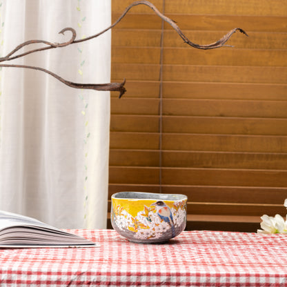 Kutani bird and wild cherry matcha bowl on a red gingham tablecloth beside an open book.