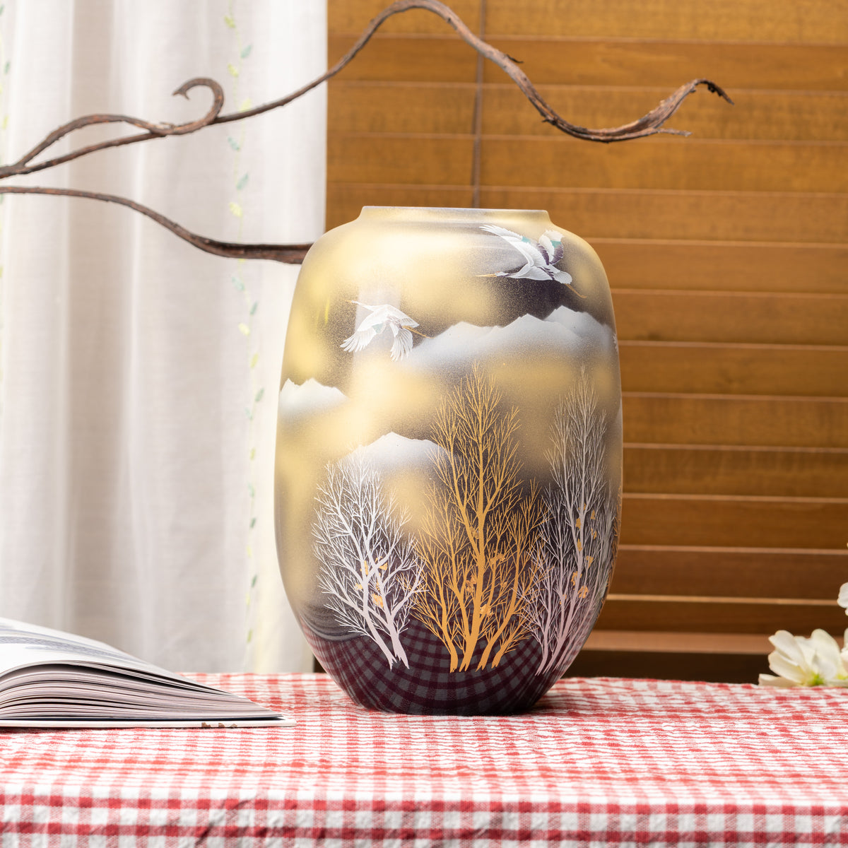 Crane and woodland Kutani vase displayed on a red gingham tablecloth beside a window.