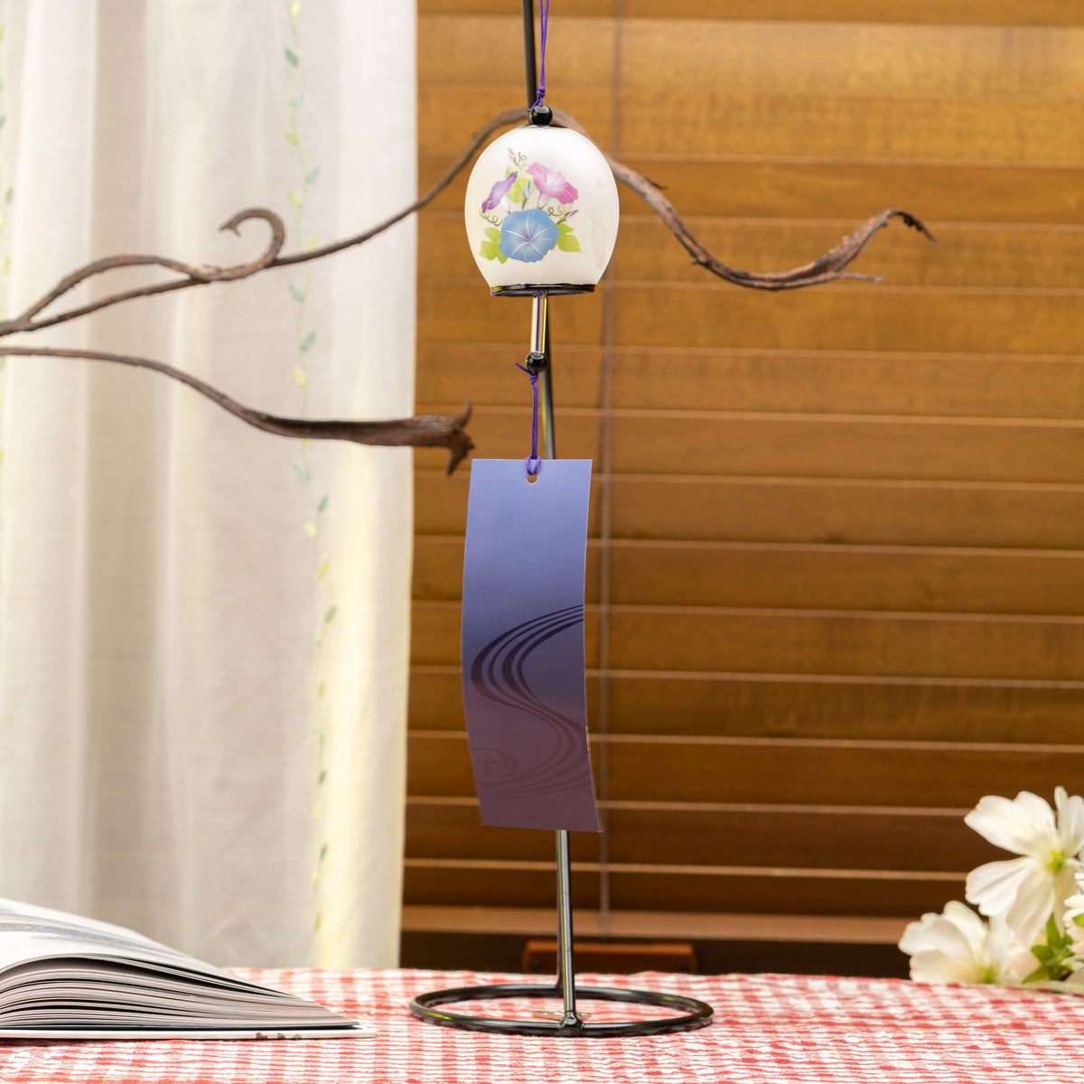 Morning glory glass wind chime hanging from a branch, with a long purple paper tag below.
