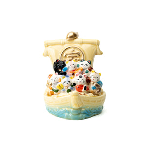 Seven colorful lucky cats aboard a yellow treasure ship with a gold-colored sail emblem and blue waves.