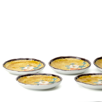 Low side view of five yellow camellia plates, showing their shallow shape and dark rims.