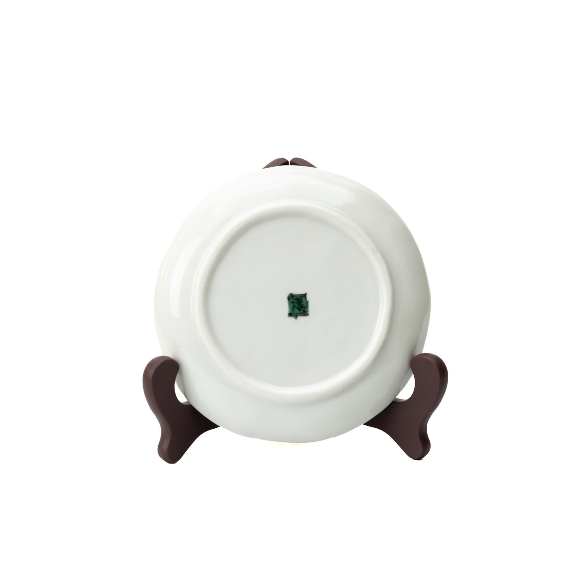 Underside of a white Kutani camellia plate on a stand, showing its circular foot and green maker's mark.