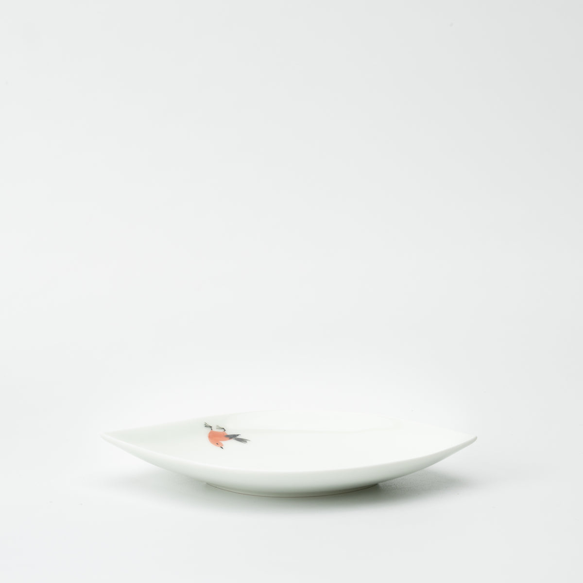 Low side view of the white Tsugumi bird leaf plate, showing its shallow curve and raised pointed ends.