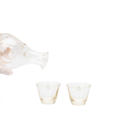Sake carafe tilted above the two matching glass cups.