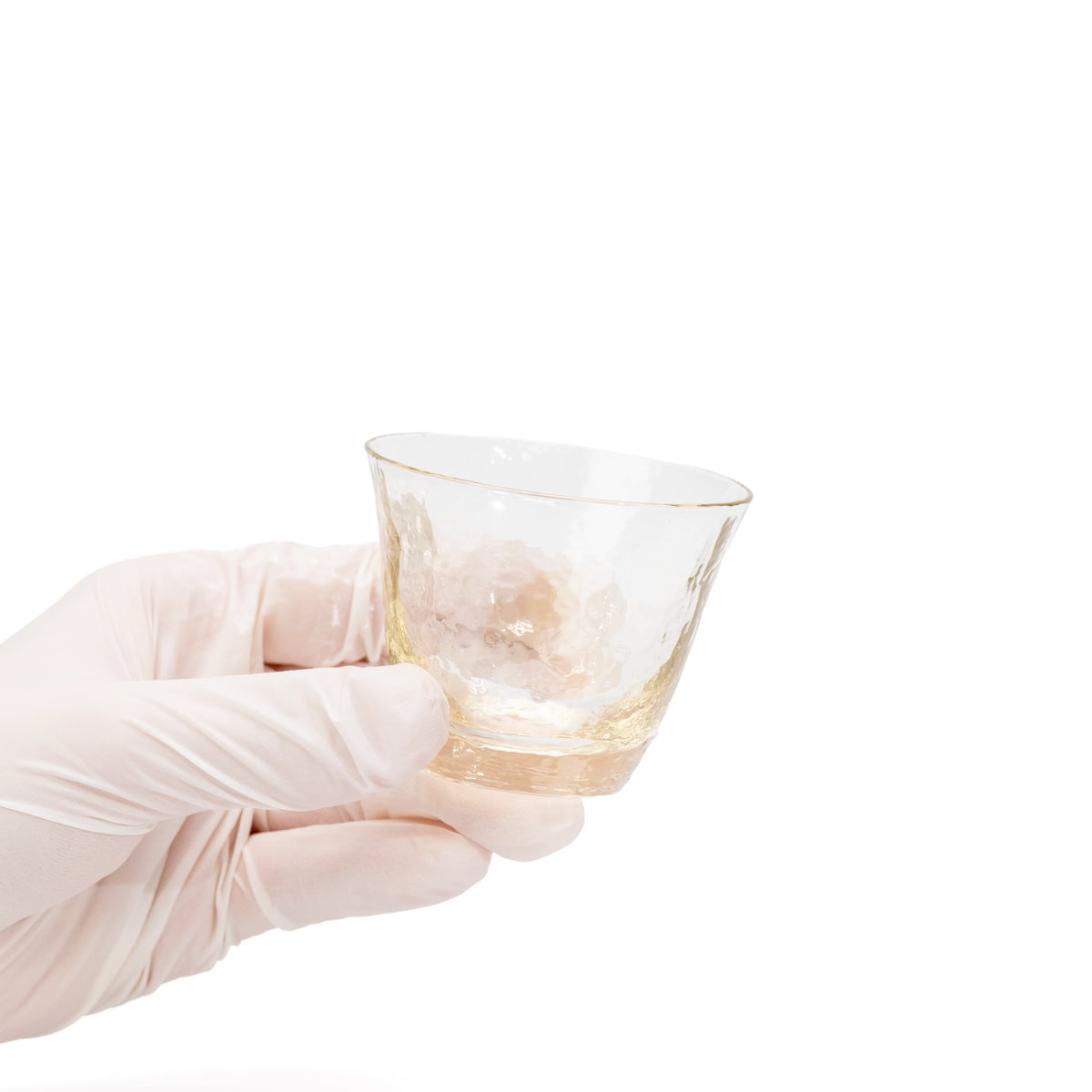 Small amber-tinted glass sake cup held in a gloved hand.