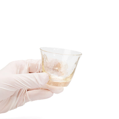 Small amber-tinted glass sake cup held in a gloved hand.