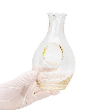 Glass sake carafe held in a gloved hand, showing its round ice pocket.