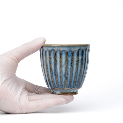 Blue-gray ribbed tea cup held in a gloved hand.
