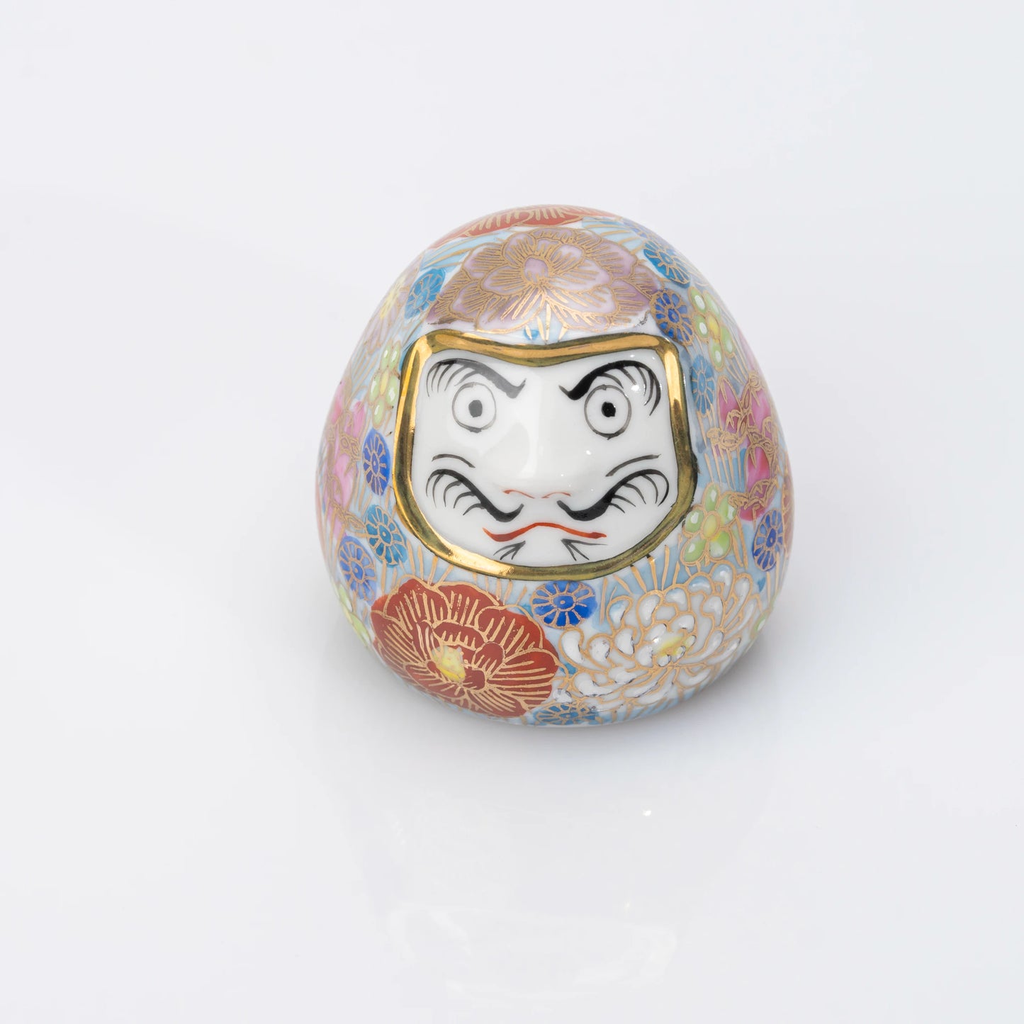 Front view of a blue Kutani porcelain Daruma with a dense multicolored Hanazume floral design and gold-tone outlines