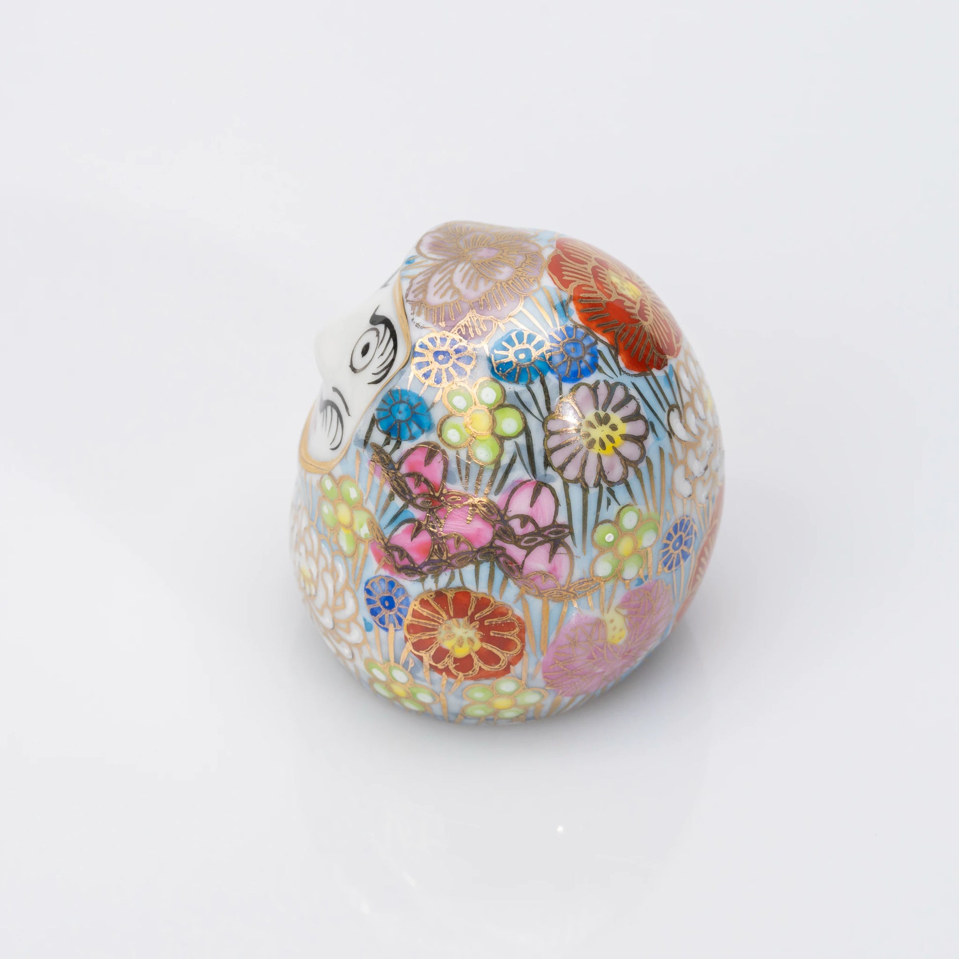 Left-side view of the blue Kutani Daruma, the floral pattern continuing around the porcelain body