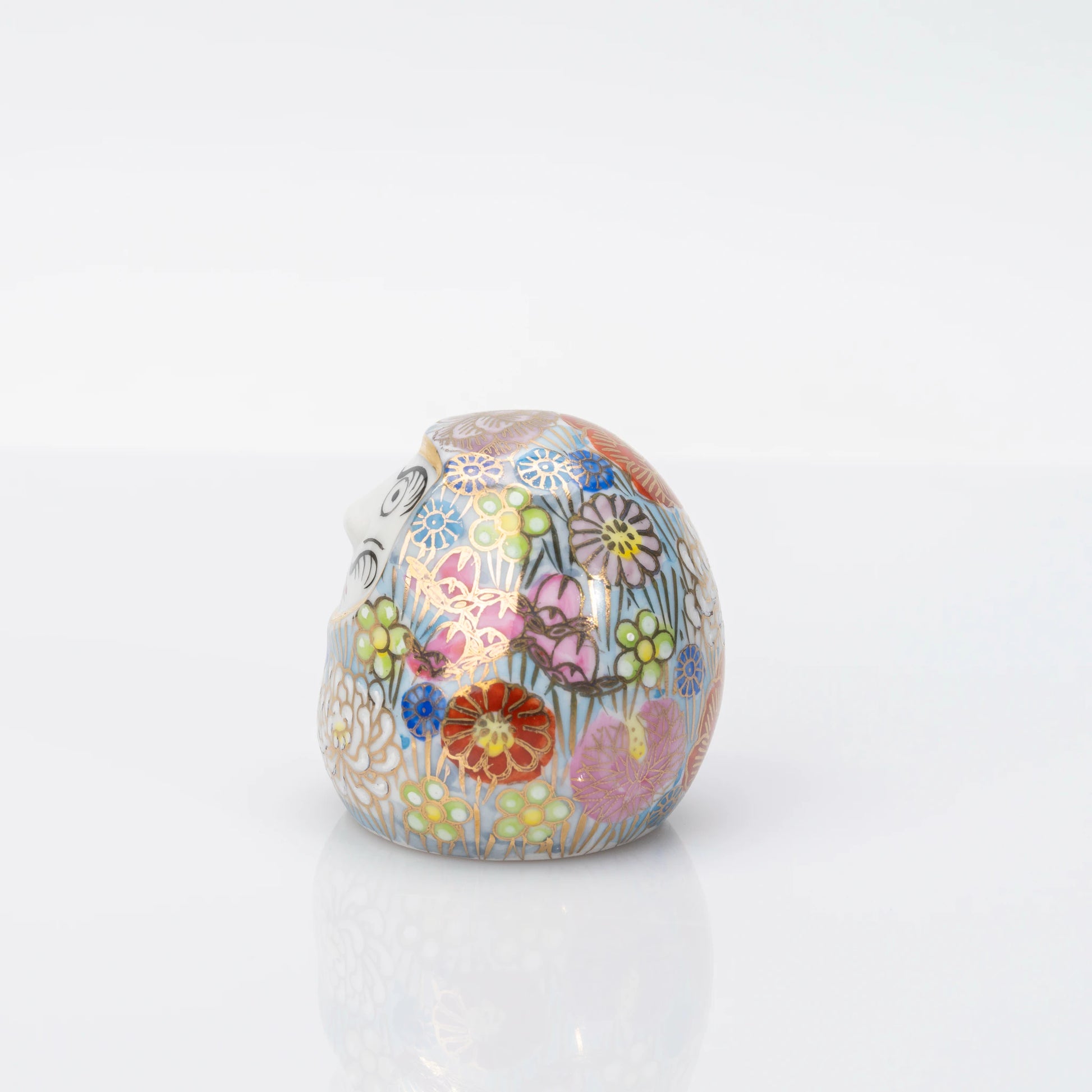 Side profile of the rounded Kutani porcelain Daruma in pale blue with floral decoration