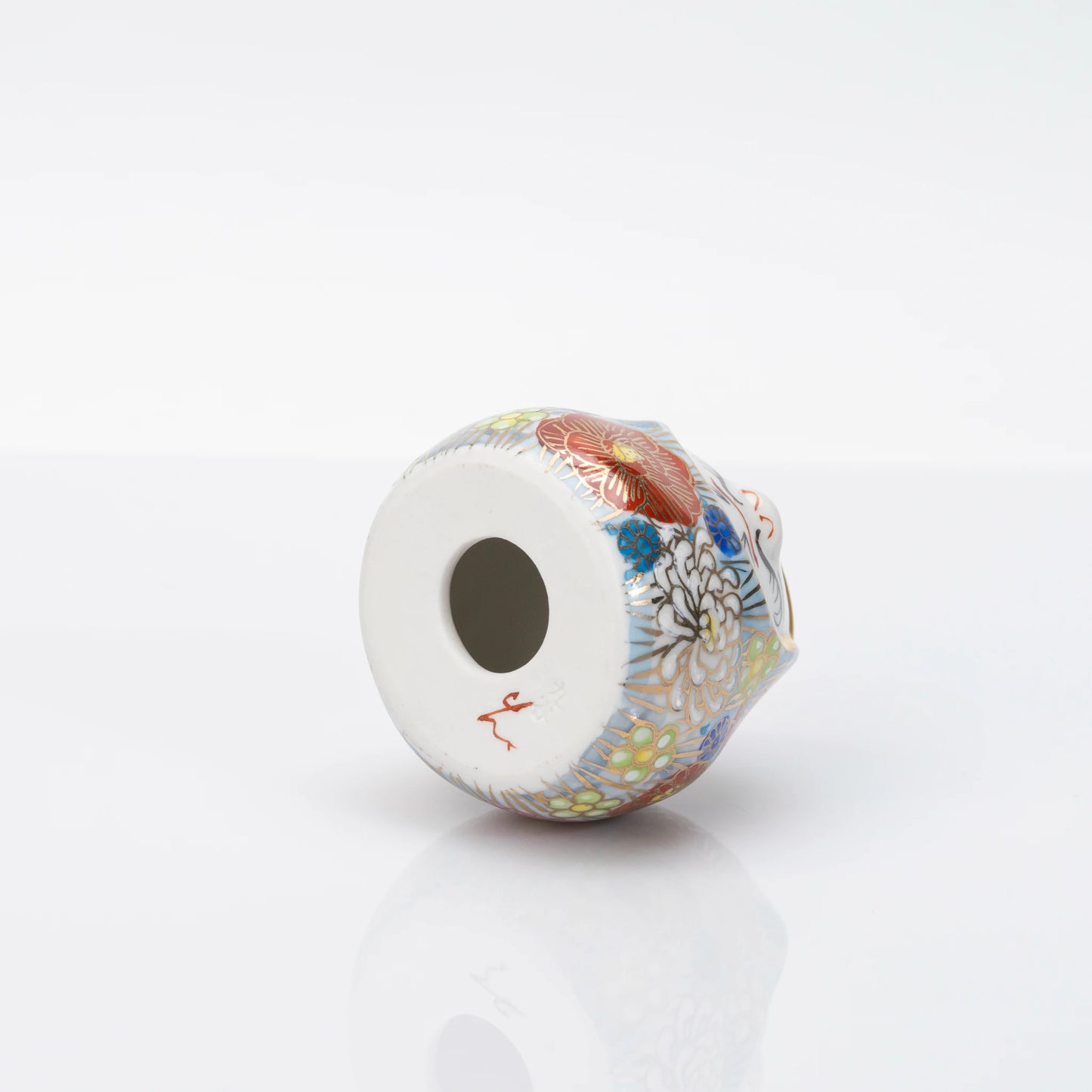 Underside of the Kutani Daruma showing the hollow circular base opening and a red mark
