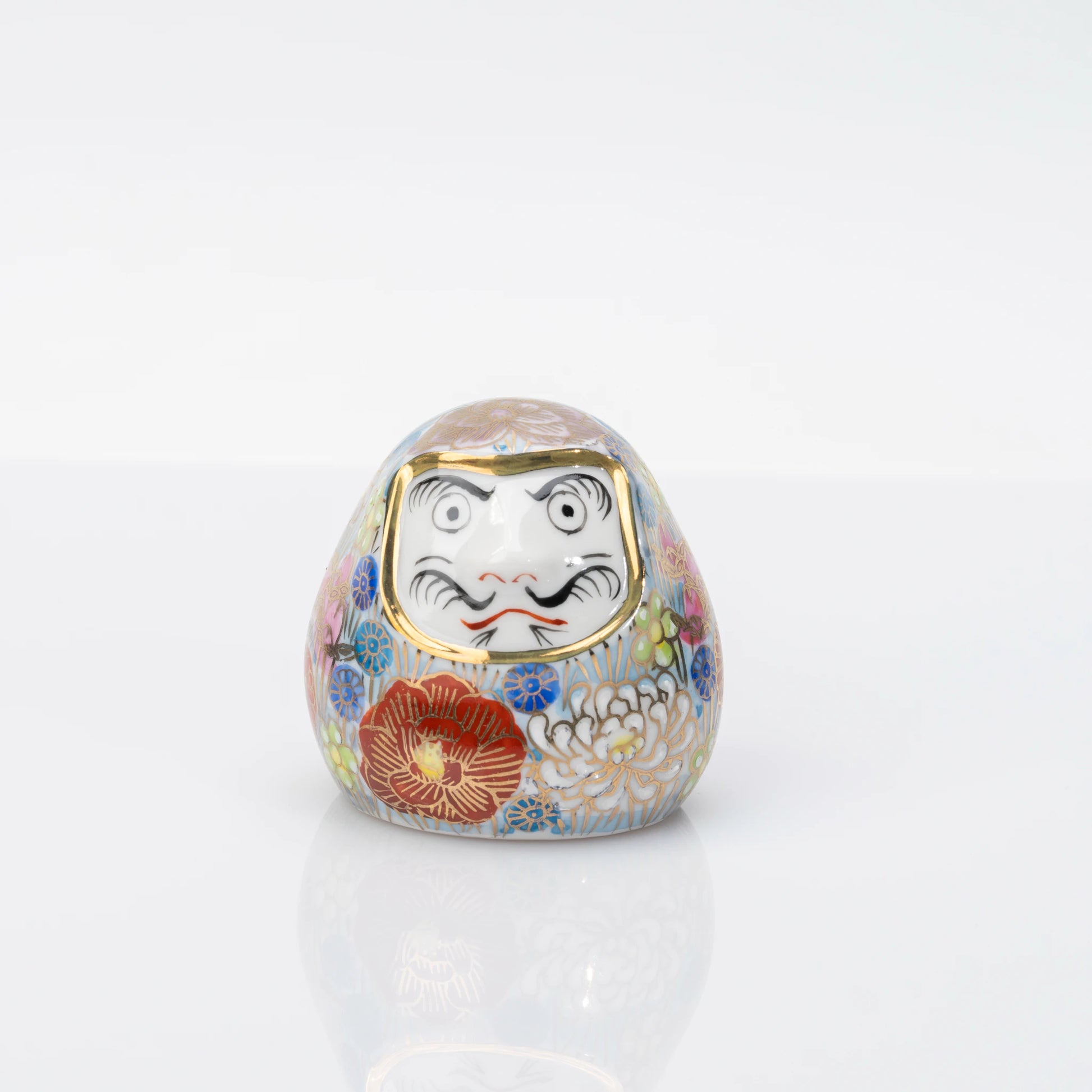 Straight-on view of the white Daruma face framed in gold tone and surrounded by floral decoration