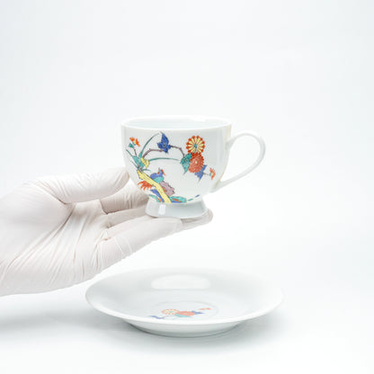 Porcelain cup with chrysanthemums and birds held in a gloved hand.