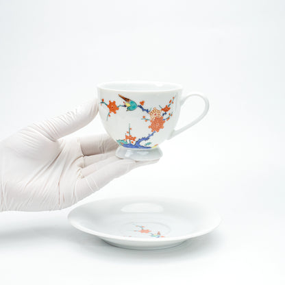 Porcelain cup with plum blossoms and a bird held in a gloved hand.