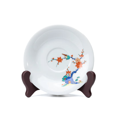 White porcelain saucer with plum blossoms and a bird, viewed from above.
