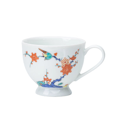 White porcelain cup with plum blossoms and a bird, viewed from the side.