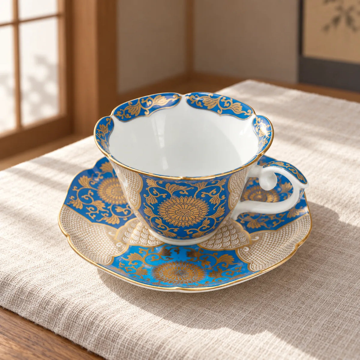 Blue-and-gold Arita chrysanthemum cup resting empty on its matching saucer in soft window light.