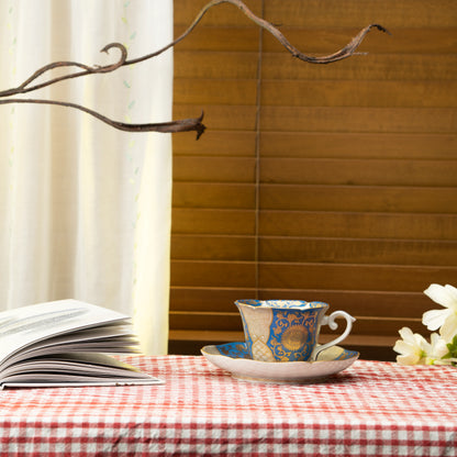 Blue and gold cup and saucer on a red checked tablecloth beside a book.