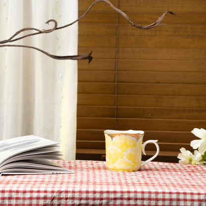 Yellow peony mug on a red checked tablecloth beside a book.
