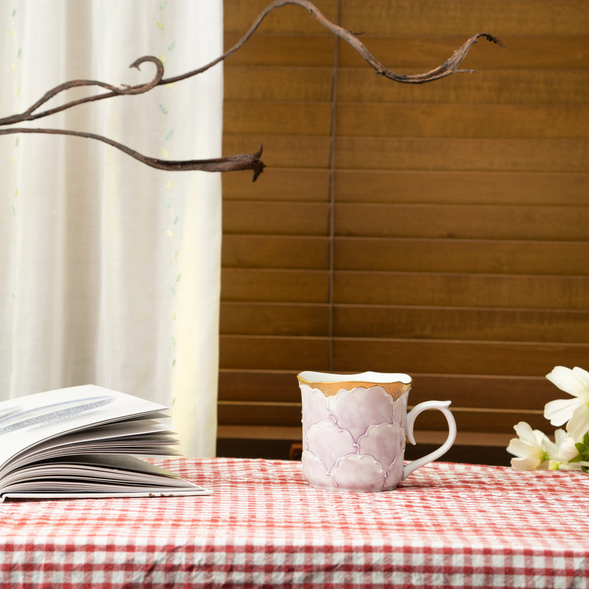 Purple peony mug on a red checked tablecloth beside a book.