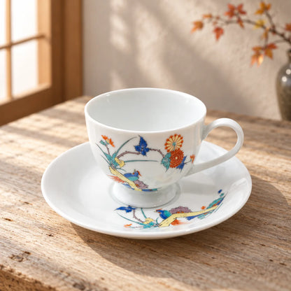 Hand-painted Arita chrysanthemum and bird cup resting empty on its matching saucer beside a warm window.