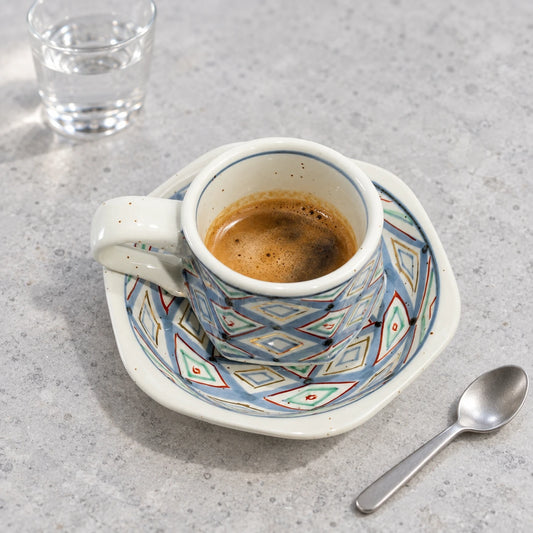 Arita diamond-patterned demitasse with espresso on its matching hexagonal saucer, beside a small spoon and water glass.