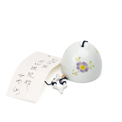 White porcelain wind chime with yellow and purple flowers and a paper strip on white.