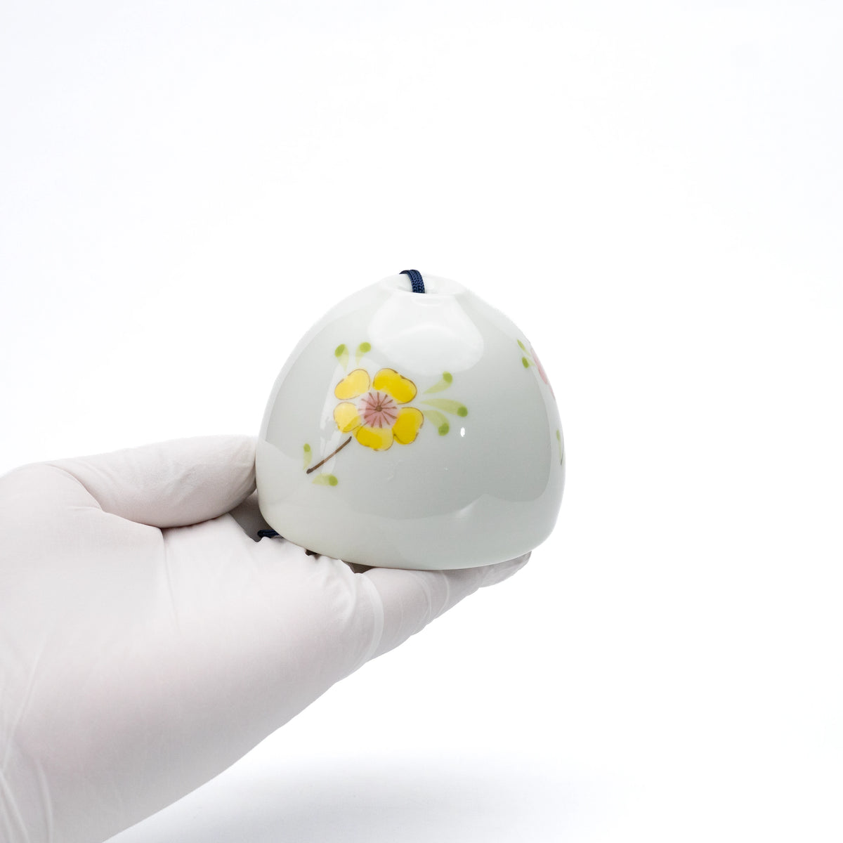 Yellow and purple floral porcelain wind chime held in a gloved hand.