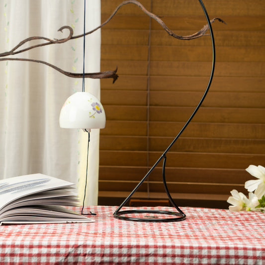 Floral porcelain wind chime hanging from a display stand on a red checked tablecloth.