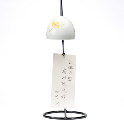 Floral porcelain wind chime and paper strip hanging from a black display stand on white.